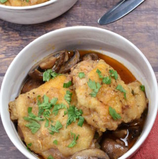 Two chicken thighs with mushrooms and sauce garnished with parsley.