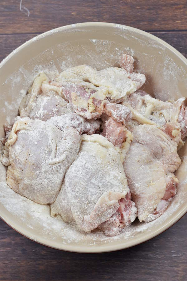 Chicken thighs coated with flour in a mixing bowl. 