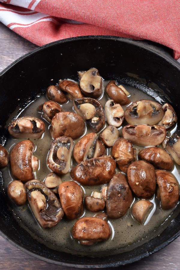 Sauteed cremini mushroom halves in a cast iron skillet. 