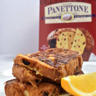 Three slices of panettone French toast garnished with an orange slice with the panettone box in the background.