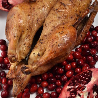 Whole roast duck arranged with cranberries and pomegranates on a serving platter.
